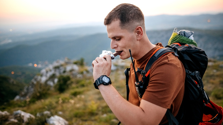 A hiker walking and eating a protein bar.