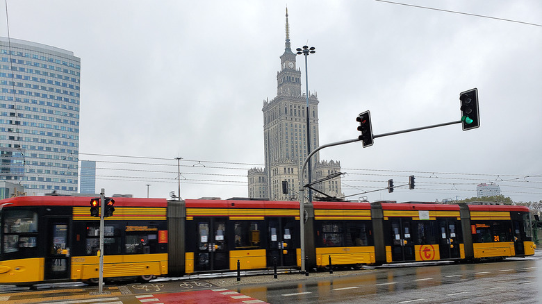 A yellow and red street tram with a tall skyscraper