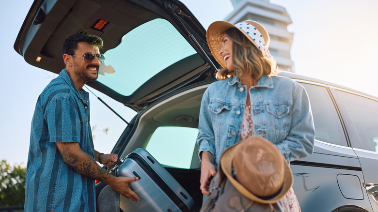 Travelers happily removing luggage from car trunk