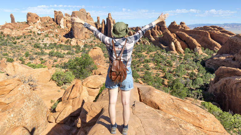 a woman standing with arms outstretched overlooking arches national park in Utah