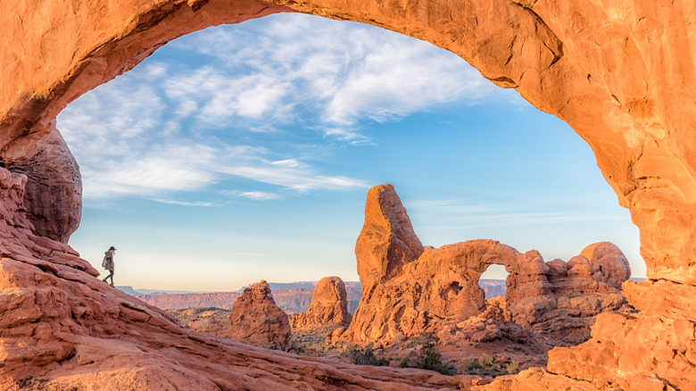 a lone hiker walks among the arches of Arches National Park in Utah
