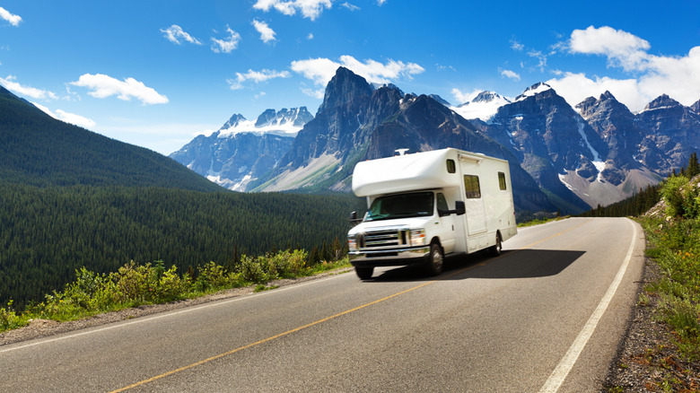 A white motorhome driving down a decline in the Rocky Mountains of Canada.