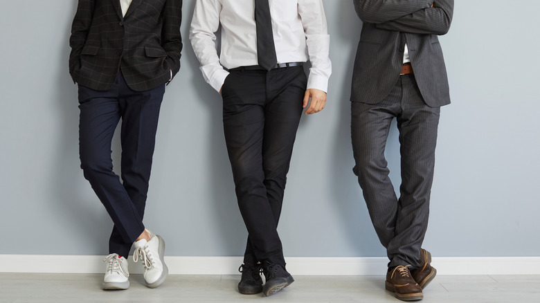 three men leaning against a wall with hands in pocket