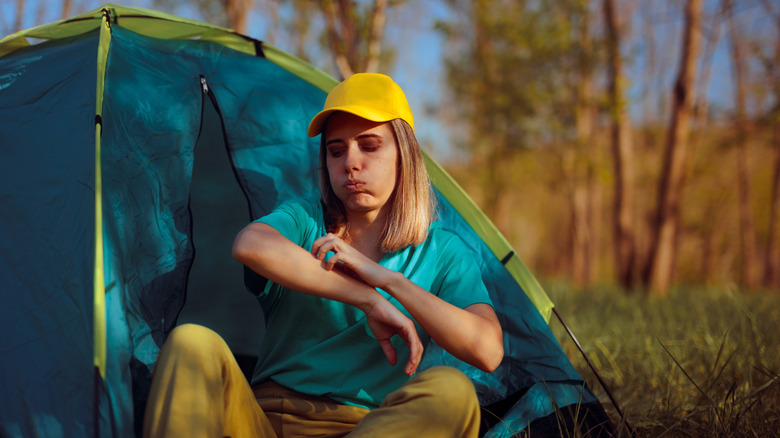 A woman at a tent scratching mosquito bites.