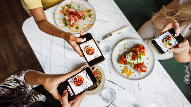 Patrons use phones to photograph their meals in a restaurant