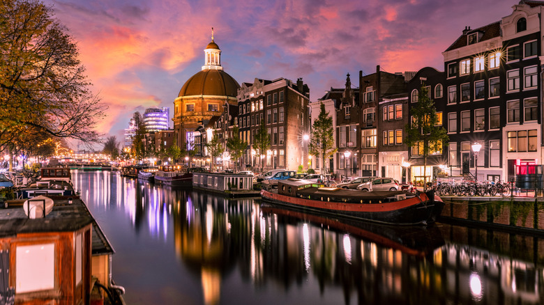 Scenic view of Amsterdam canal at sunset with historic buildings and boats reflecting on the water.