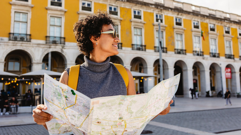 Smiling tourist is holding a map and wearing a yellow backpack while visiting the beautiful city of Lisbon in Portugal