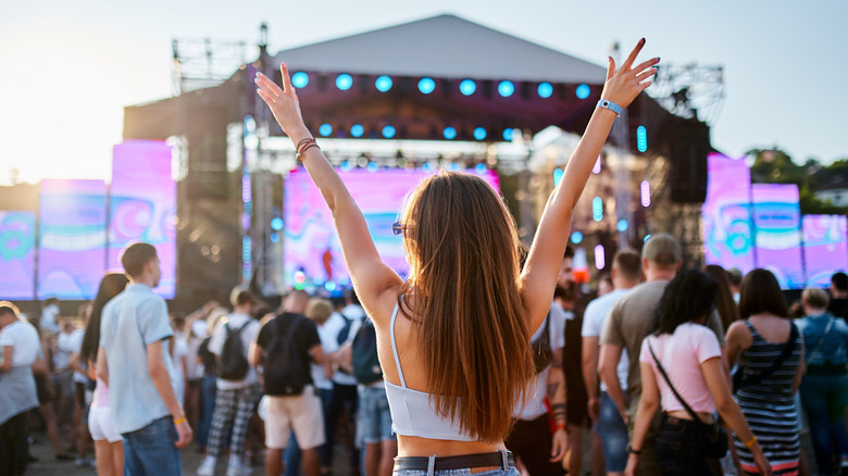 Back view of a crowd and a woman with her arms raised at a concert