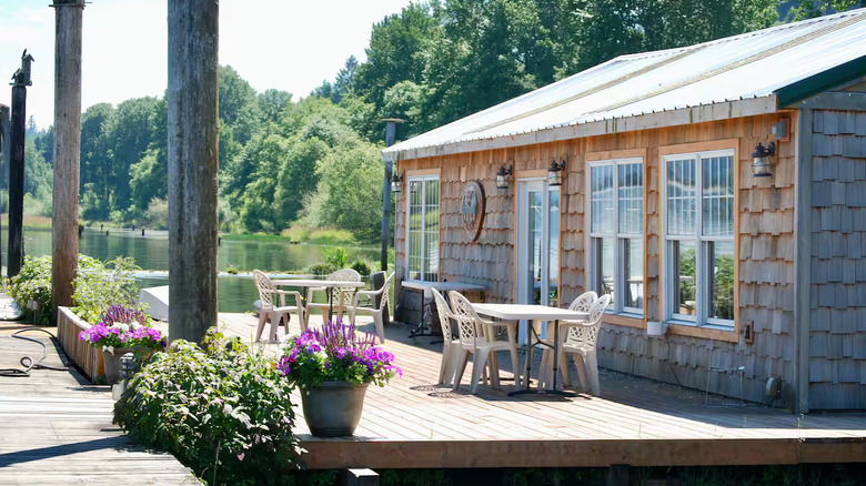 A house on a dock with two outdoor tables on the dock and pots of flowers