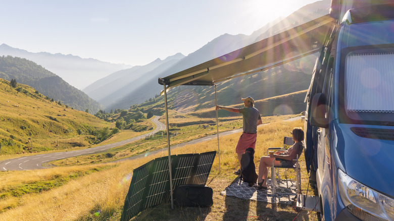 A couple sitting by camper van with solar panels.