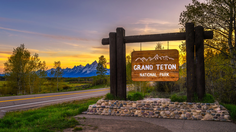 A Grand Teton National Park sign in front of a mountain landscape at dusk