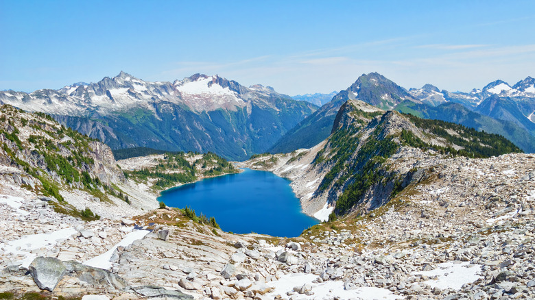 A rocky mountain top with a lake and a mountain range in the background