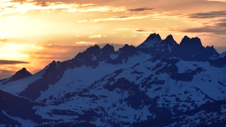 Aerial view of a jagged mountain range covered in snow with the sun setting behind