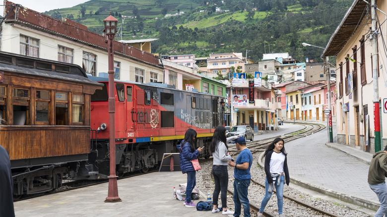 People on the street mill around a set of train tracks in Ecuador