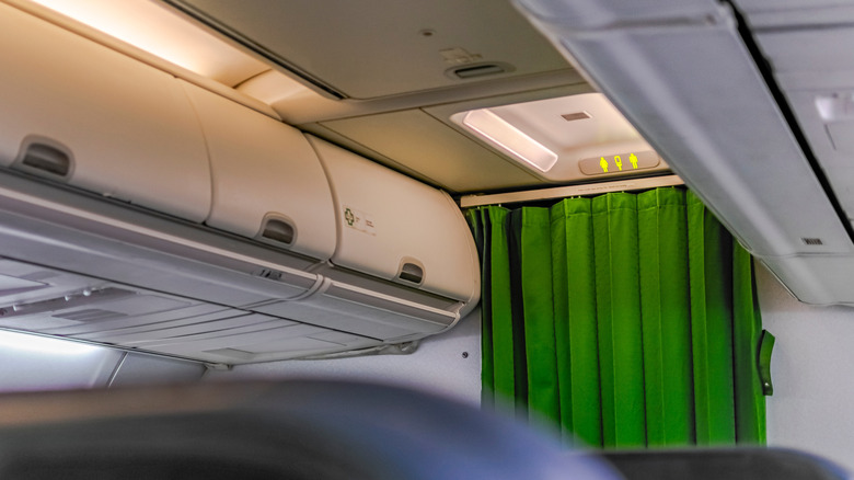 Airplane interior facing bathroom area, green curtain