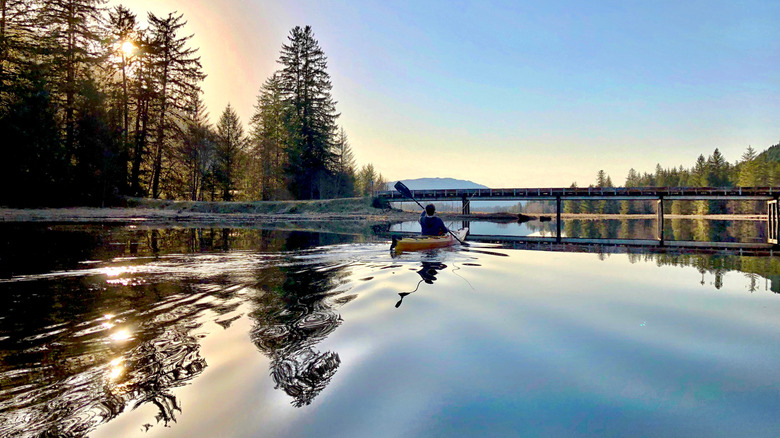 A man kayaking in golden hour toward a bridge on a lake near Petersburg, Alaska
