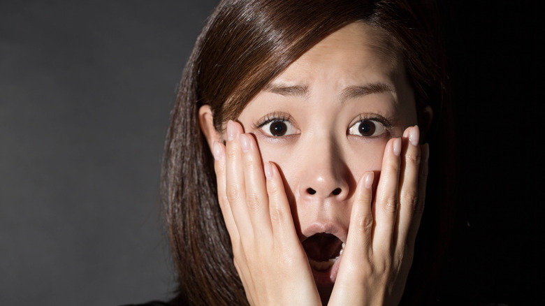 A woman looks alarmed, with hands over face