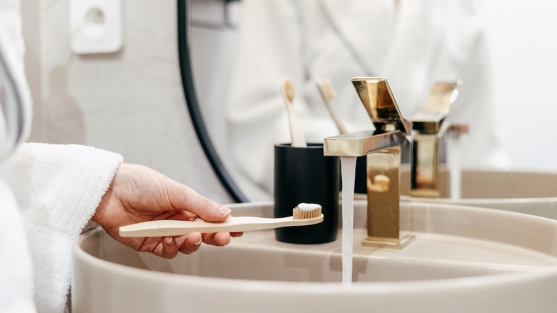 Hand holding toothbrush over sink