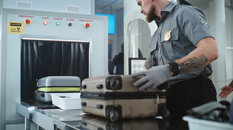 A border patrol agent placing a suitcase into an x-ray machine.
