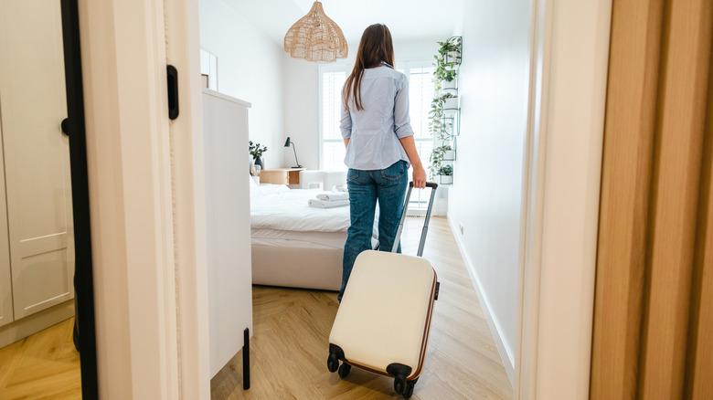 Rearview of a woman pulling luggage into a room.