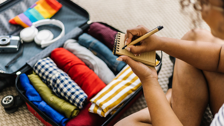 Person packing suitcase and writing on checklist