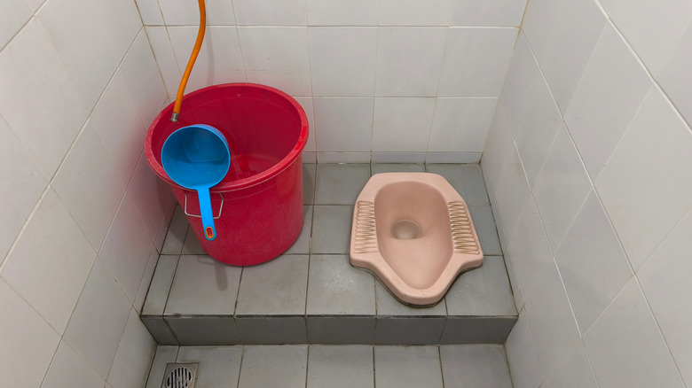 A squat toilet next to a bucket.