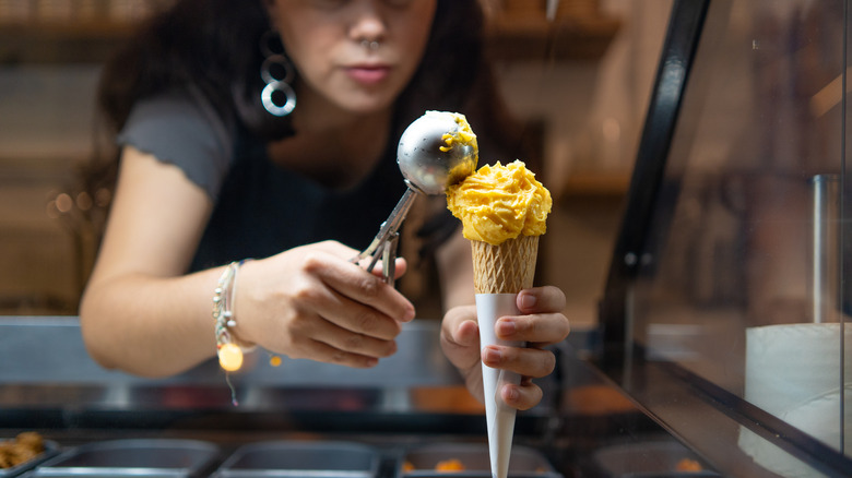 A worker scooping gelato into a cone.