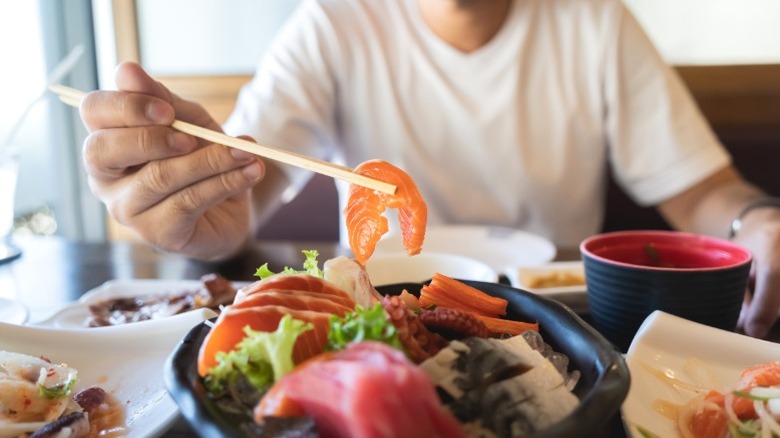 person using chopsticks to pick piece of meat from dish at restaurant table