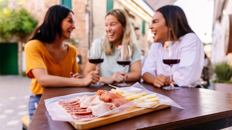 Three women sitting at a table enjoying a glass of red wine with a cheese board