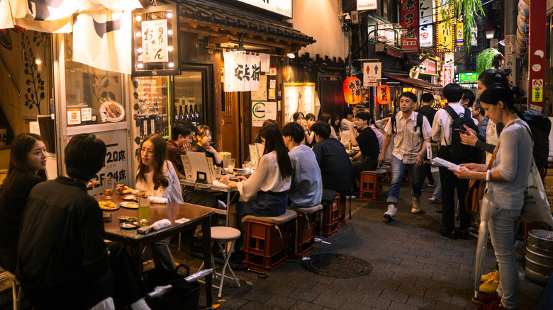 Tourists and locals enjoying drinks and food in a small alley in Japan