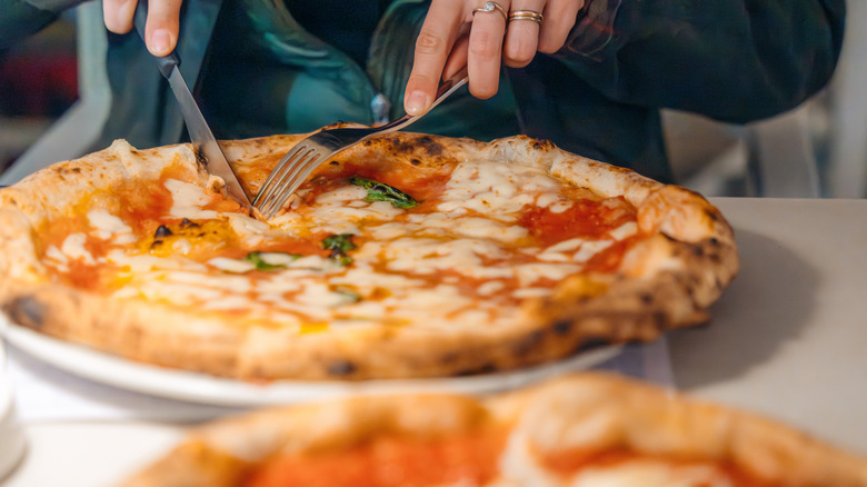 person cutting a personal pizza pie into slice with a fork and knife