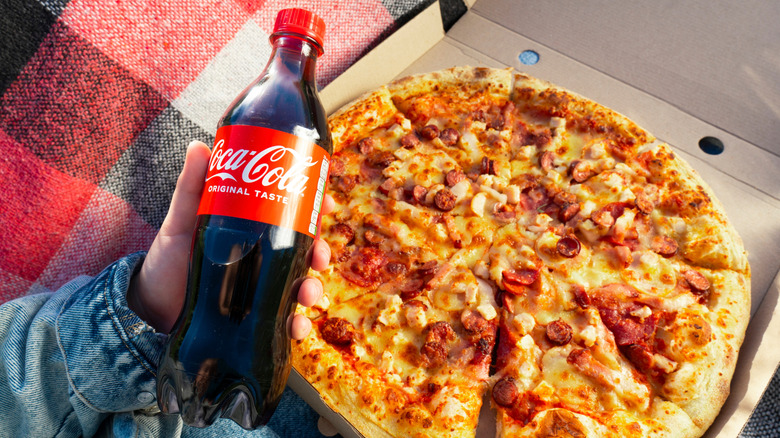 person holding a bottle of coca-cola and a box of pizza