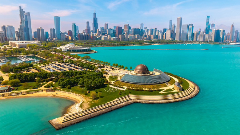 An aerial view of Adler Planetarium in Chicago bordered by blue water, with tall buildings in the background