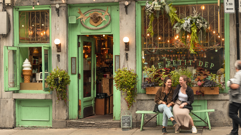 Two women laugh on a bench in front of a traditional cafe bistro restaurant in the Old Town Montreal