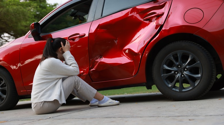 A woman sitting next to a red car involved in an accident