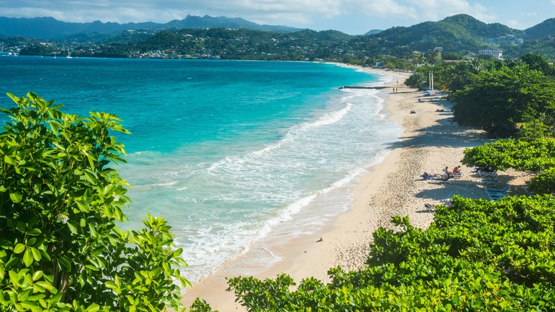 high view of a beach with turquoise water, greenery, rolling hills