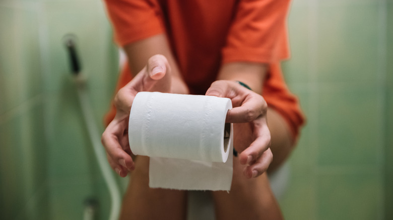 Woman on toilet holding toilet roll