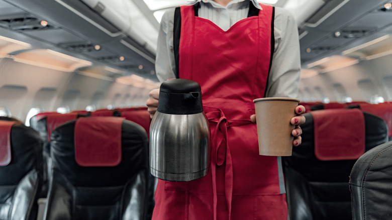 Cropped photo of stewardess holding a coffee pot and paper cup.
