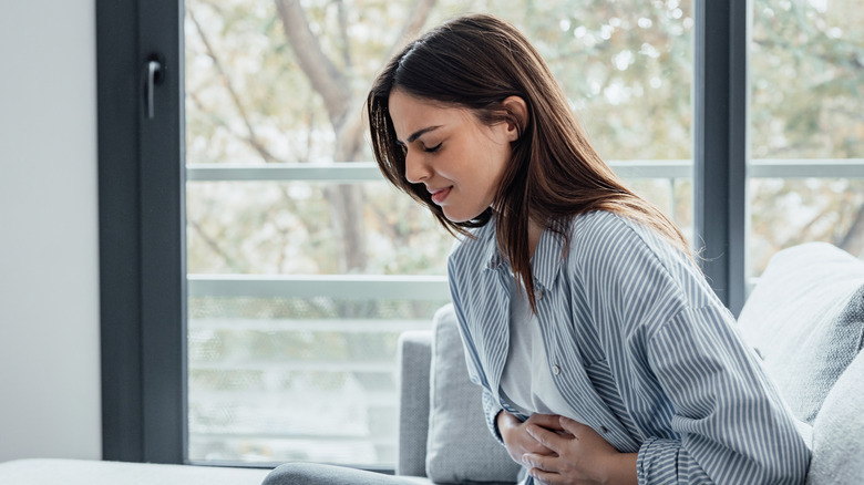 Sick young woman sat in front of a window in pain holding belly stomach