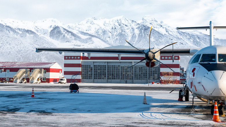 Small airplane at a snowy airport with snow-covered mountains in the background