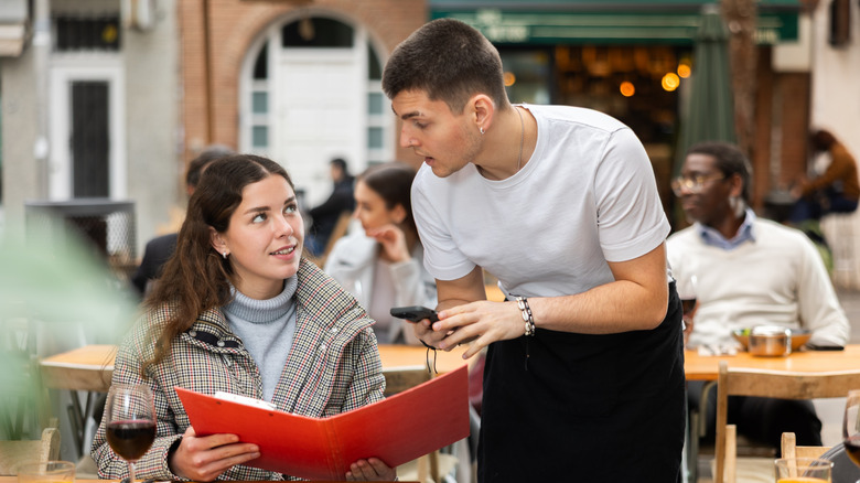 Male waiter takes an order from a young woman on the veranda of a restaurant.