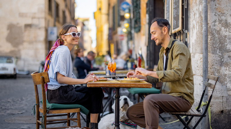 Man and woman eating pasta and drinking wine at restaurant on the street in Rome.