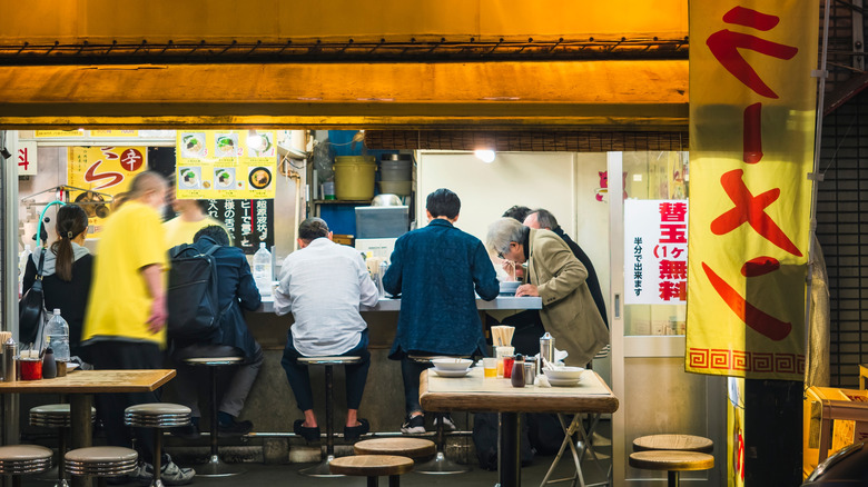Japanese noodle shop with people eating at counter in Tokyo at night.