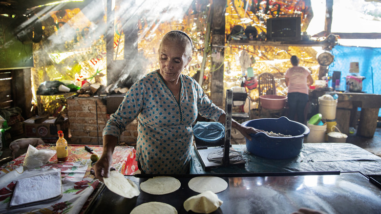 An older Mexican woman making tortillas by hand.