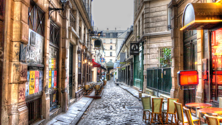 A cobblestoned alley in Paris lined with stone buildings, cafés, and outdoor seating
