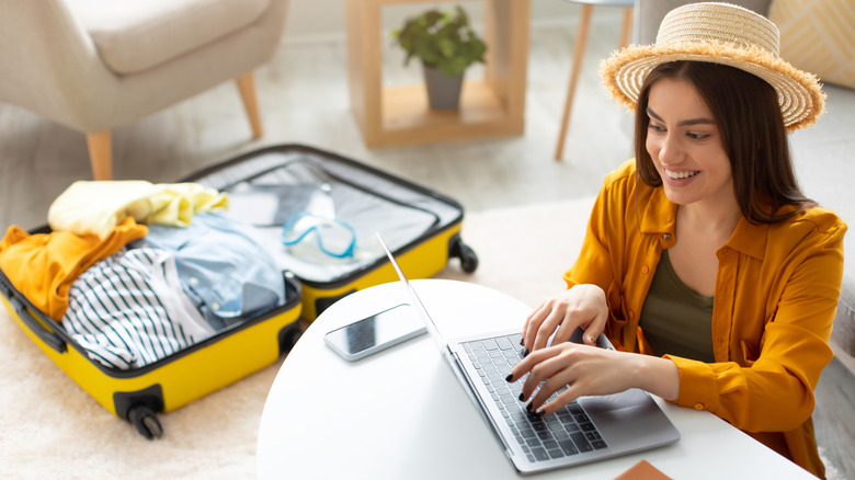 woman with suitcase booking a reservation on laptop