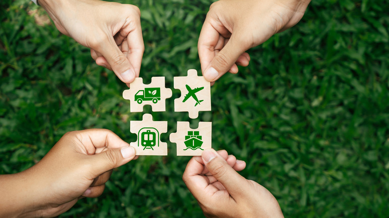 Four hands holding wooden pieces of a jigsaw puzzle depicting methods of transport to promote sustainable travel
