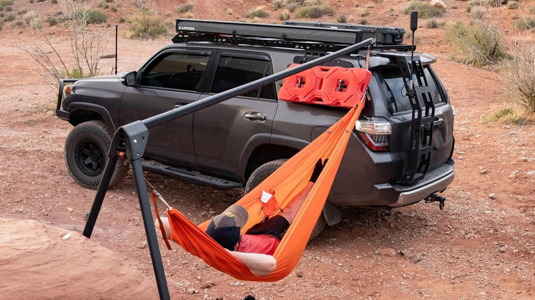 A man relaxing in a HAMMOK Outpost hammock stand attached to a car