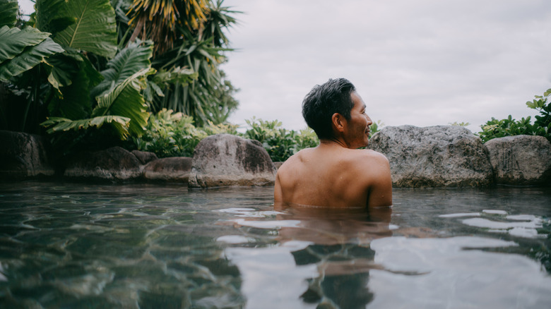 Rear view of man relaxing in outdoor hot spring bath