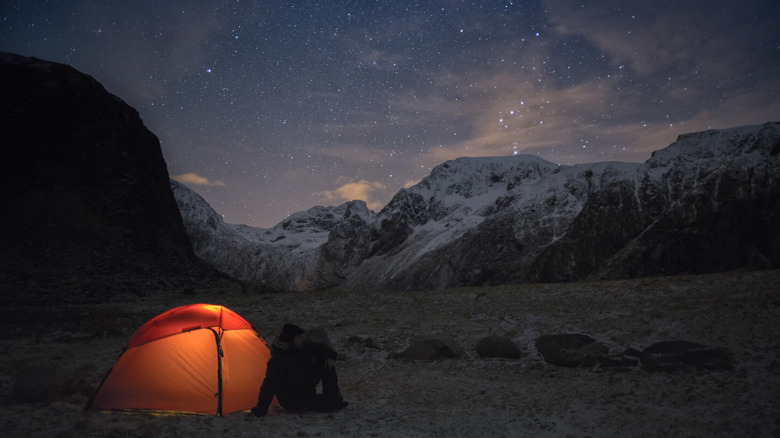 An illuminated tent in the mountains at night under a brilliant starry sky
